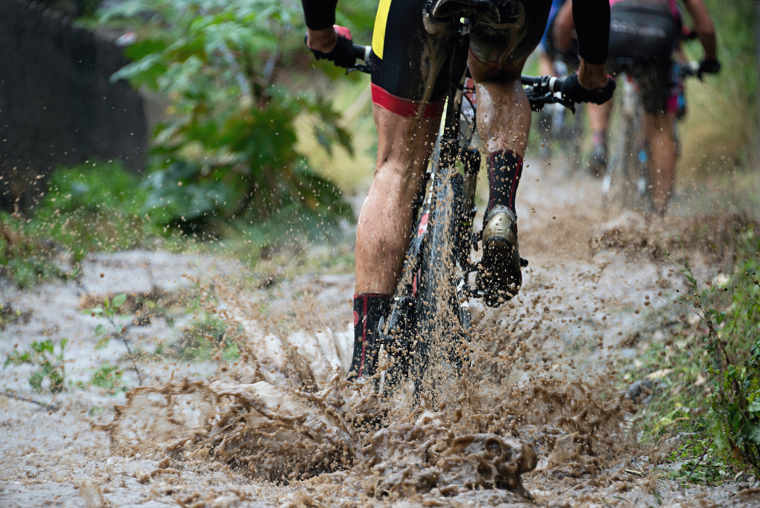 Mountain biker cycling through large muddy puddle.