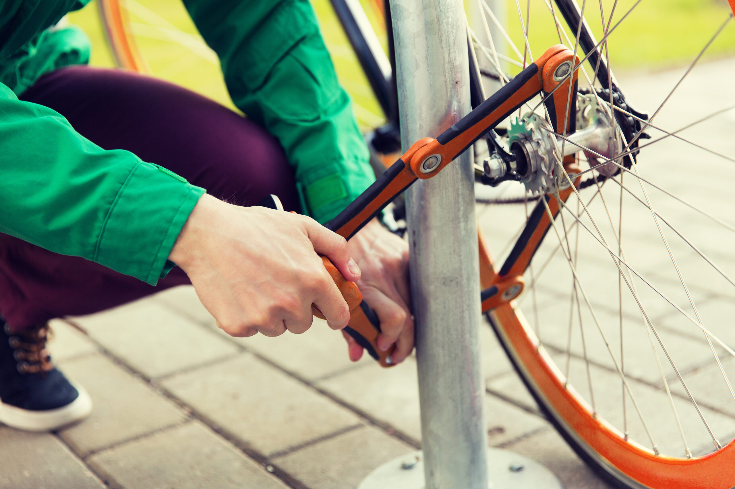 Person locking bike with orange bike lock through the frame to an immovable object.