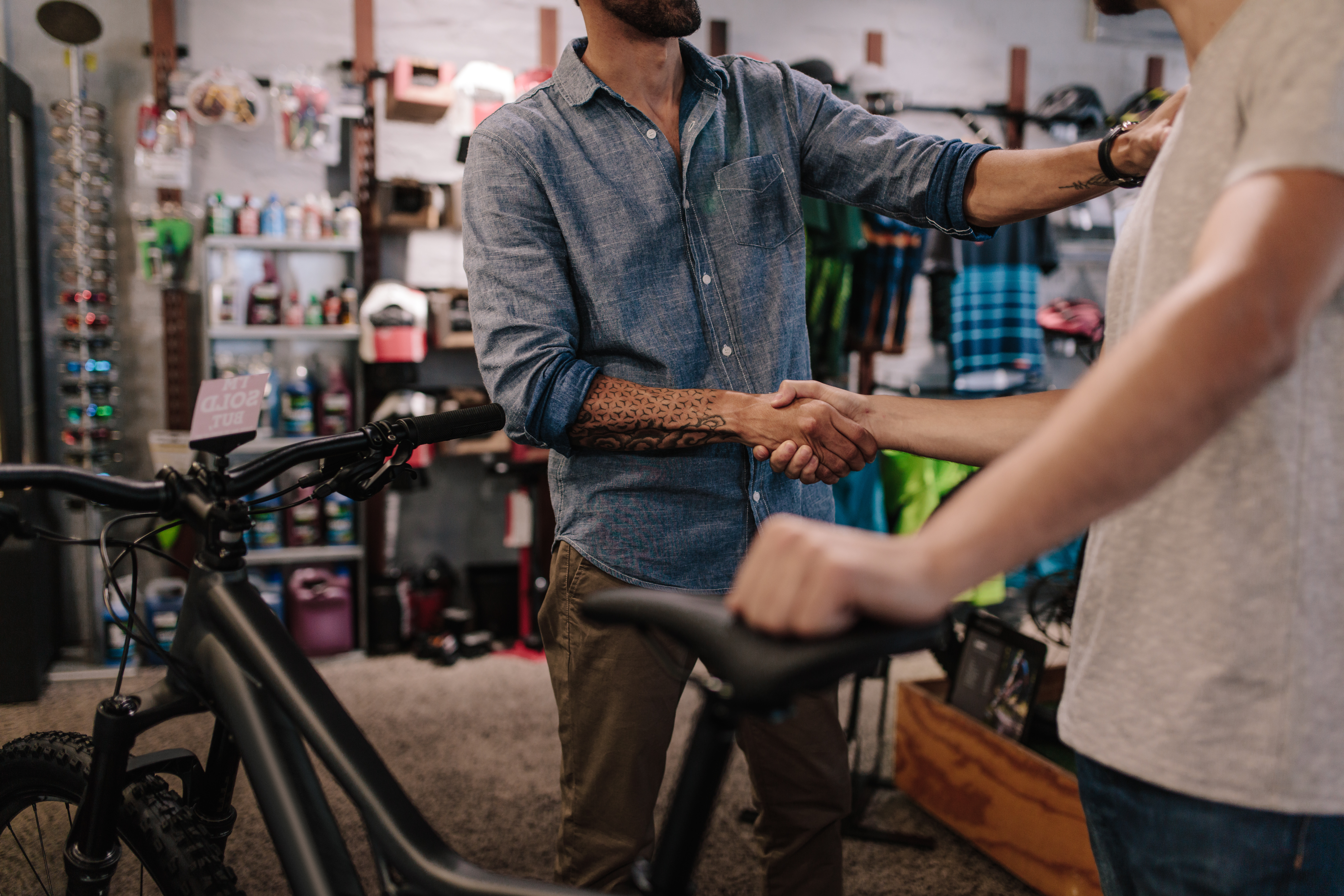 In a sports shop two men shake hands as one holds saddle of the bike he has just bought.