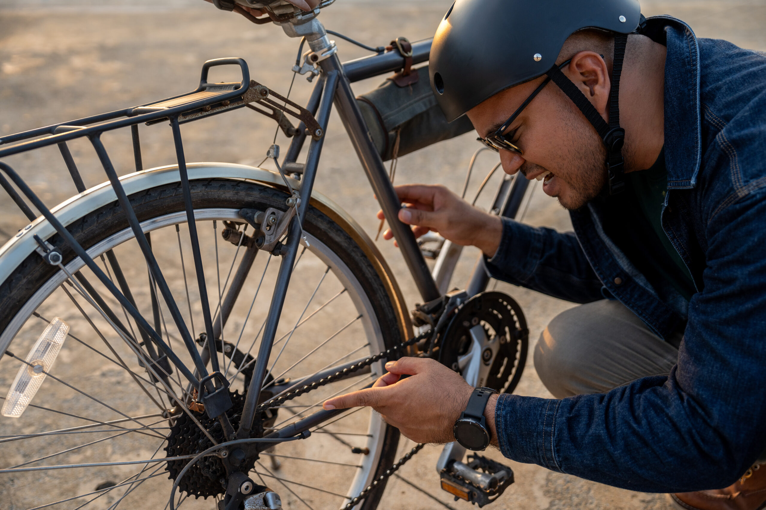 A man wearing a helmet repairs a bicycle focused on the bike's chain.